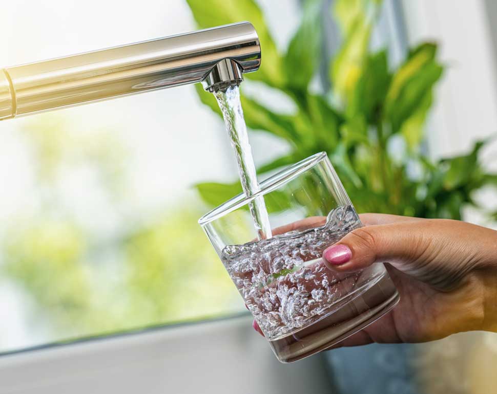En hand fyller ett glas med dricksvatten från en kran.
