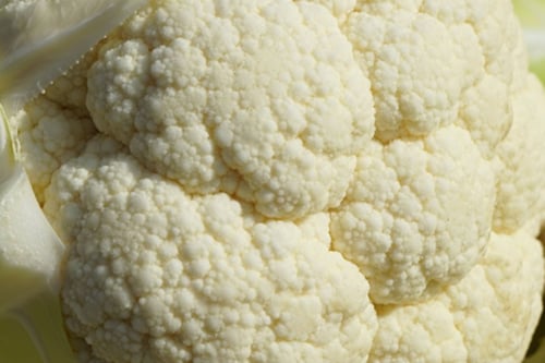 Certificación Orgánica China Flor de Coliflor fresca de color blanco con hojas verdes alrededor, colocada sobre una superficie de madera.