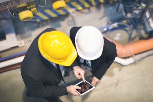 Två inspektörer, med varsin bygghjälm i olika färger, sedda ovanifrån