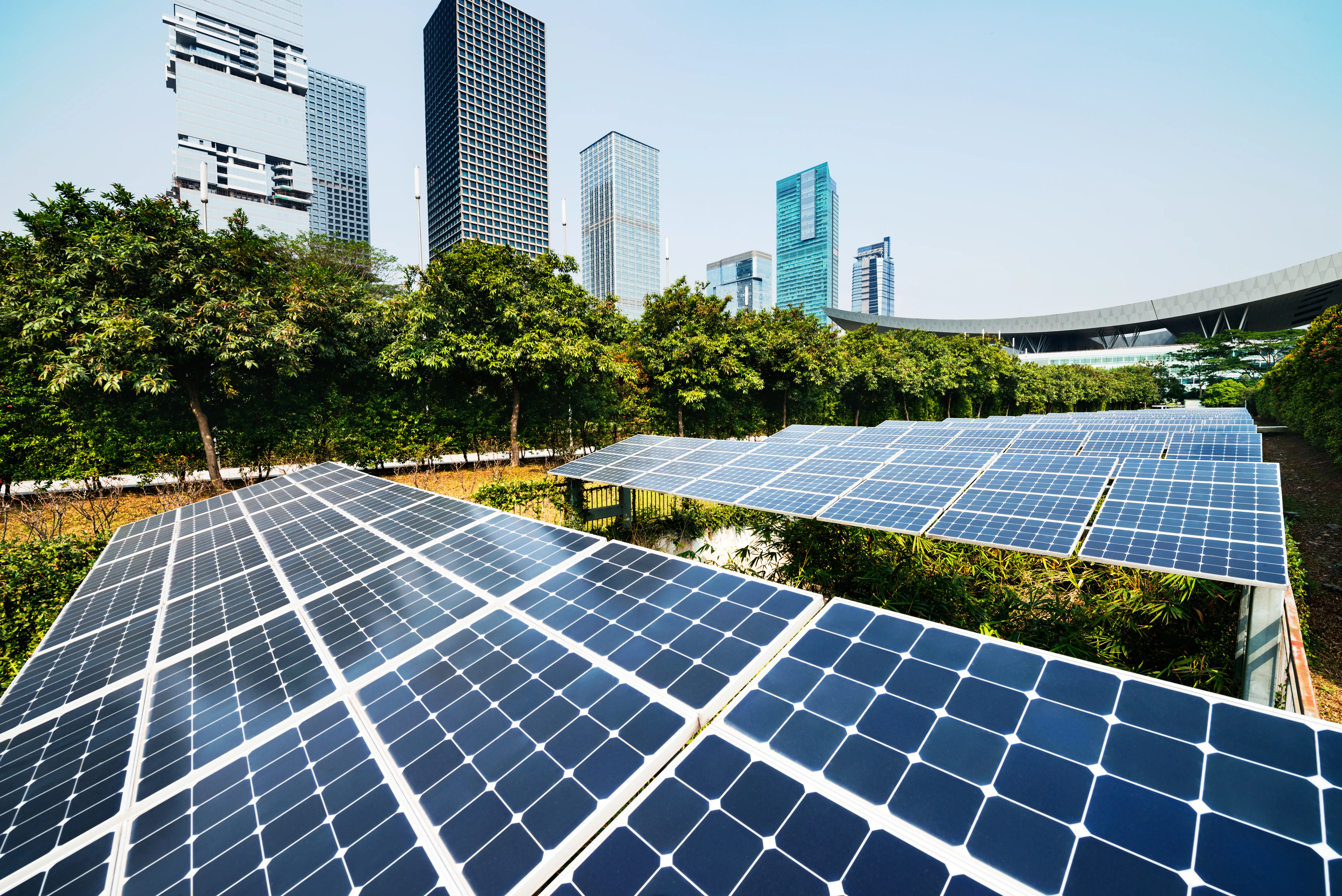Solaranlage mit Photovoltaikmodulen in einer grünen Stadtlandschaft vor modernen Hochhäusern und einem urbanen Skyline-Hintergrund.
