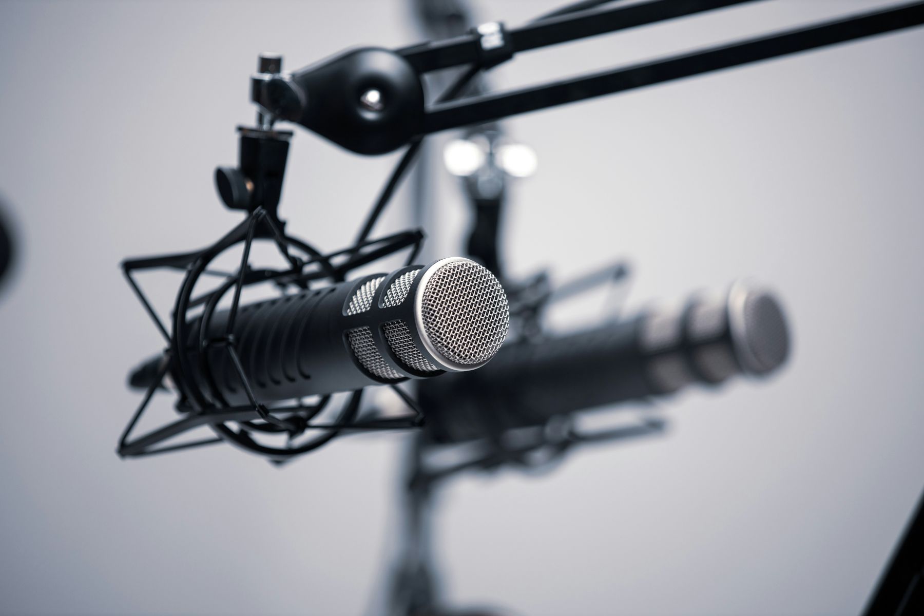 Close-up of a studio microphone mounted on a boom arm with a blurred second microphone in the background.