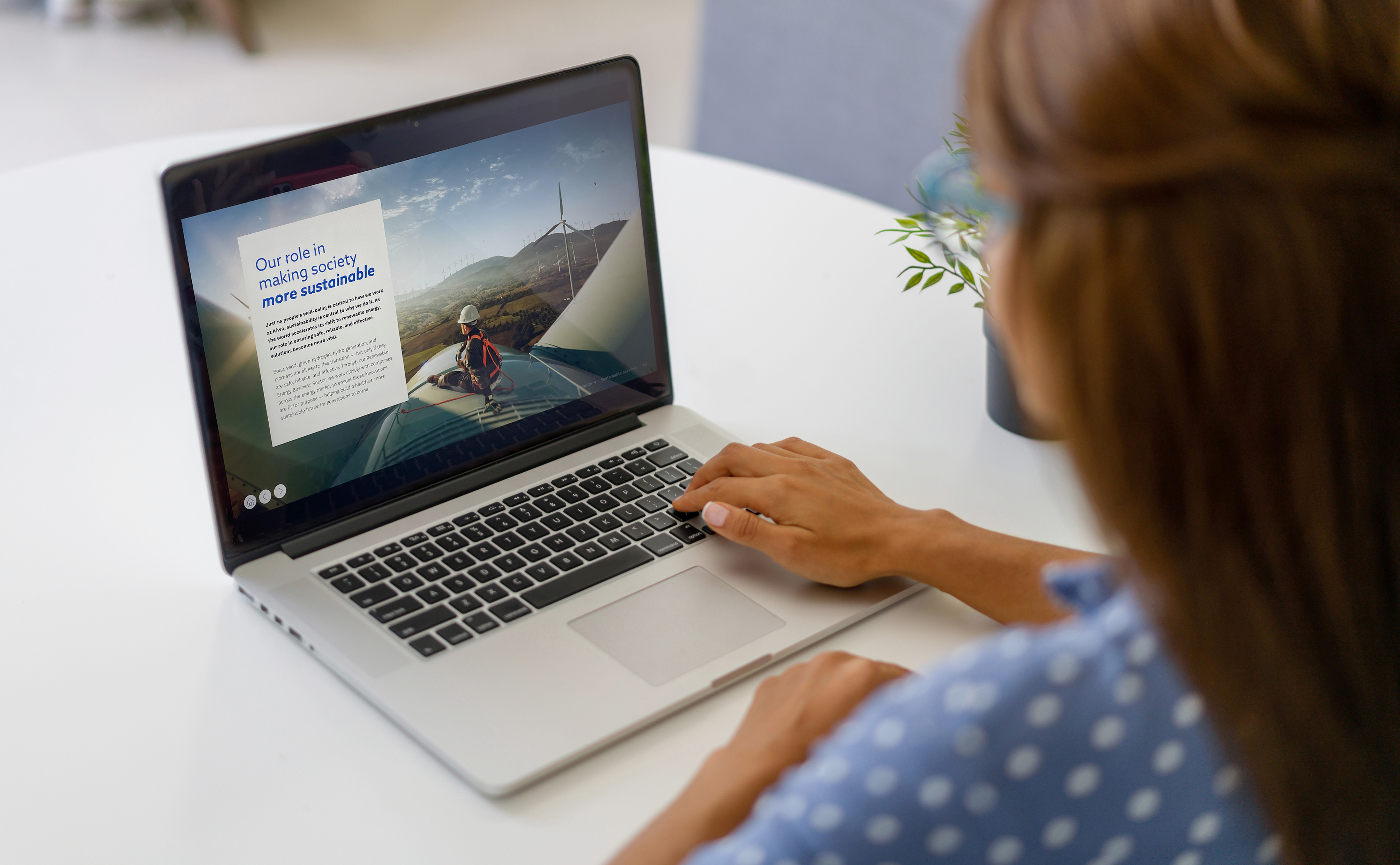 一位穿蓝色点状衬衫的女性正在使用笔记本电脑，屏幕上显示有关可再生能源的信息和图像。