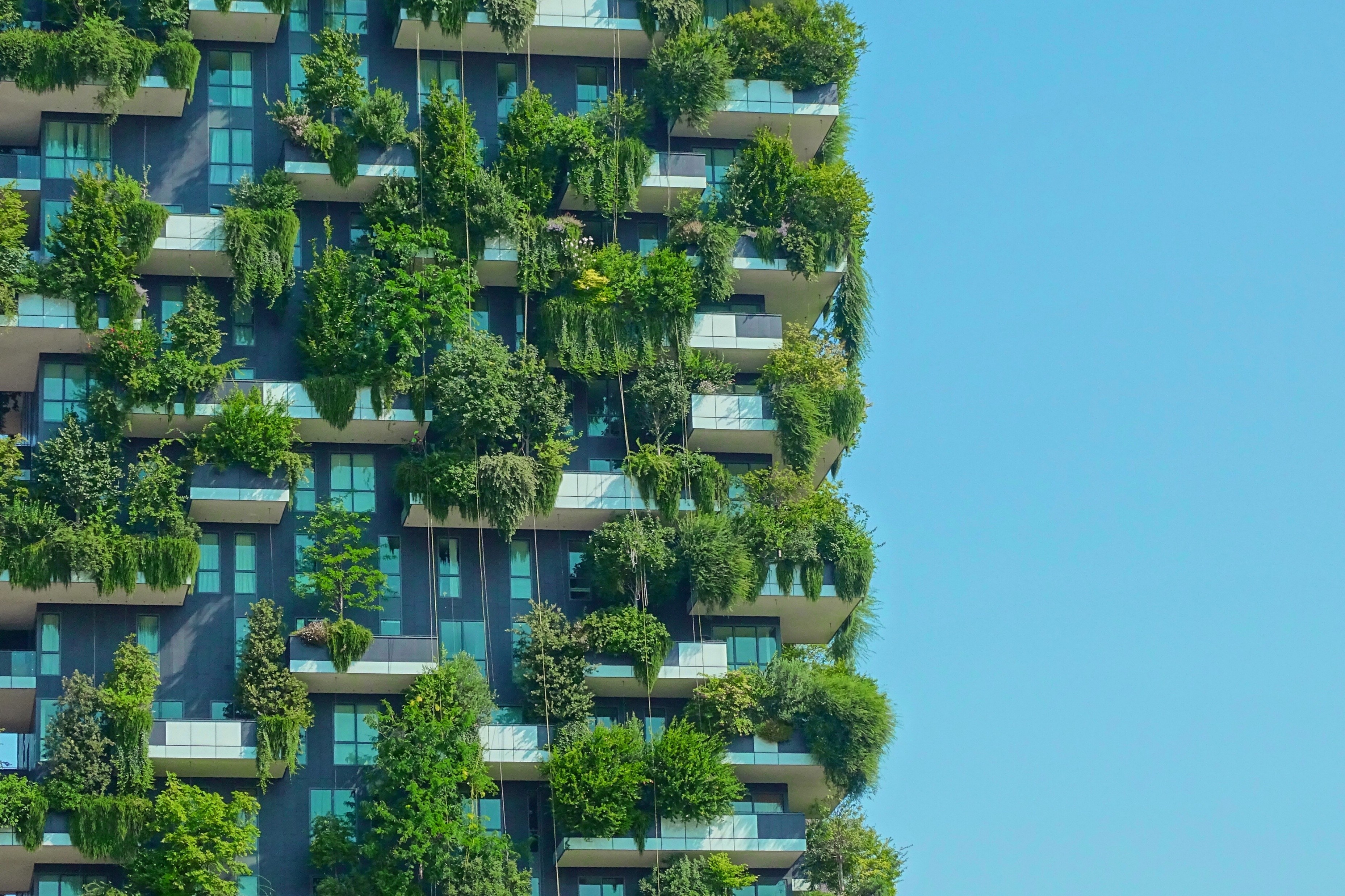 Modern apartment building facade covered in lush green vegetation and balconies against a clear blue sky.