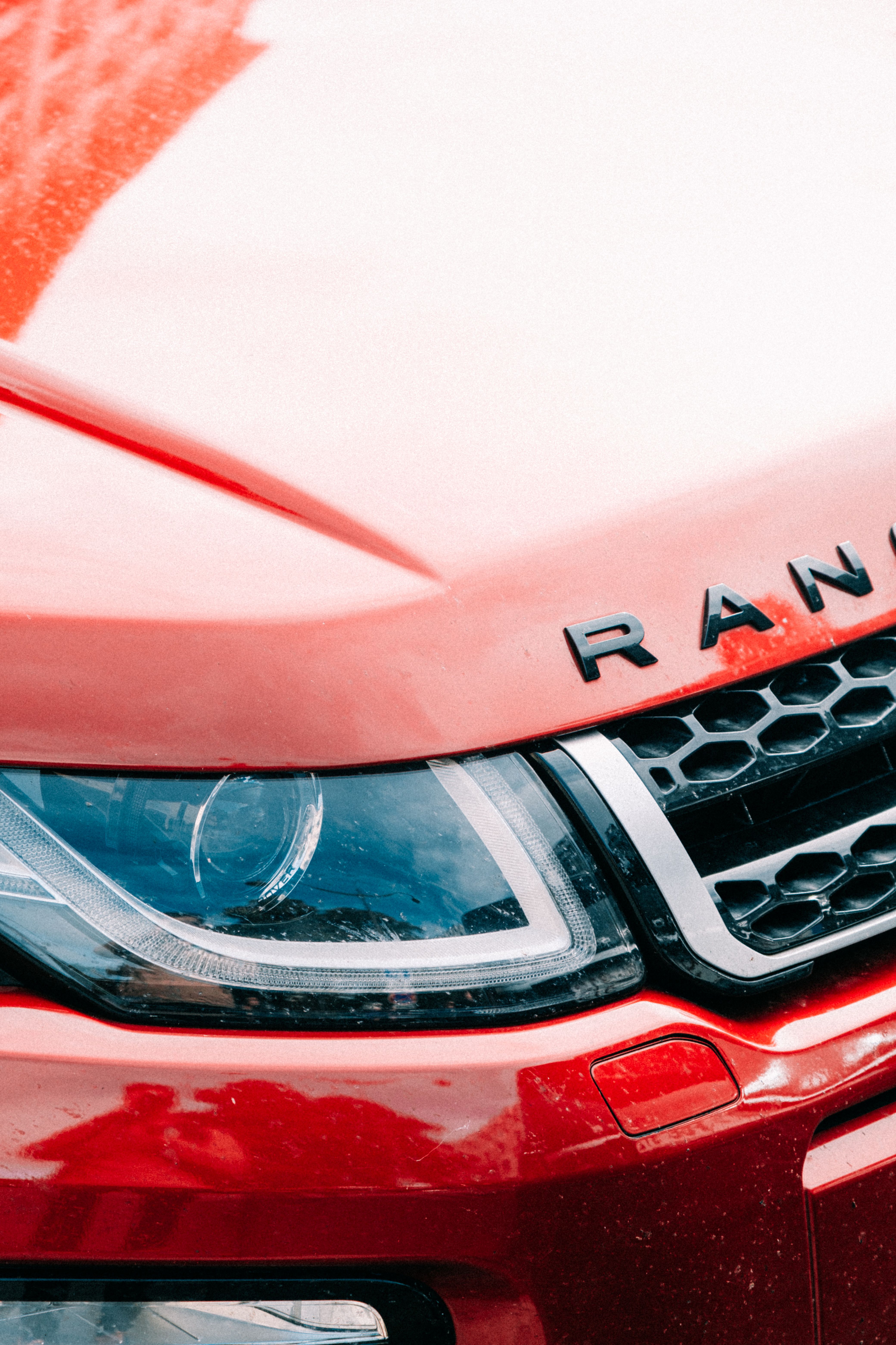 Close-up van de voorkant van een rode Range Rover met koplamp en grille|Kiwa SCM