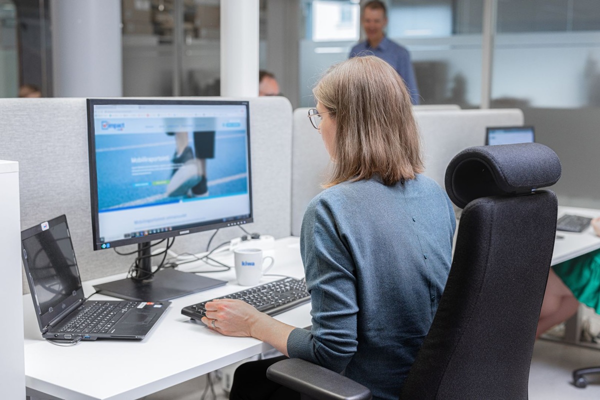 Woman working at a desk with laptop and desktop monitor in a modern office workspace.