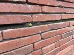Close-up van een rode bakstenen muur met een smalle horizontale voeg en een klein geel rond detail in het midden.