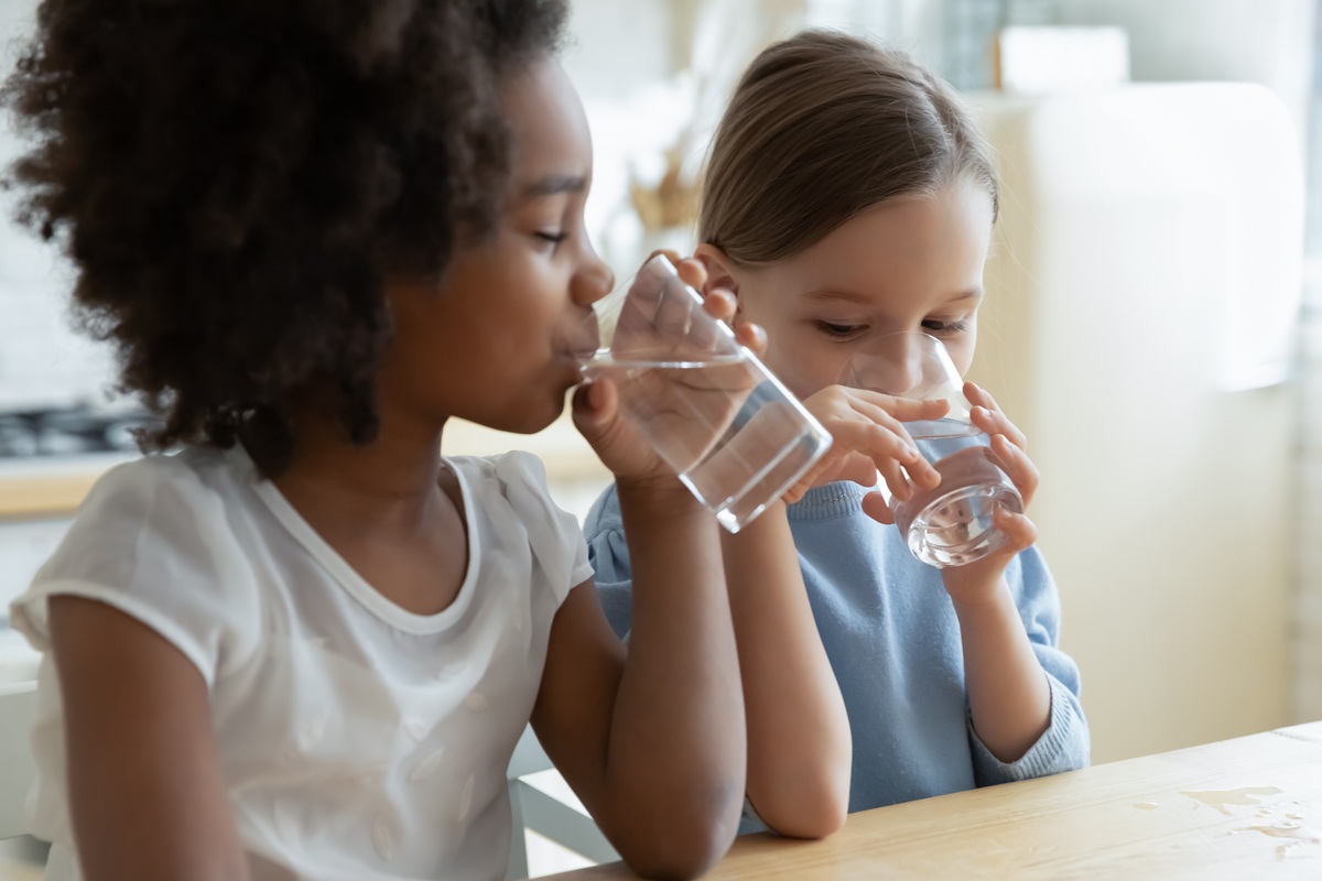 Twee kinderen drinken water aan een tafel in een keuken.