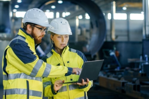 Kiwa inspectors wearing hard hats and high-visibility jackets reviewing plans on a laptop in an industrial setting