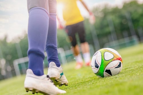 Person som spelar fotboll på en gräsplan, med fokus på fötter och en fotboll nära.