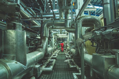 Industri där det visas många olika rörledningar kors och tvärs samt flera skorstenar.