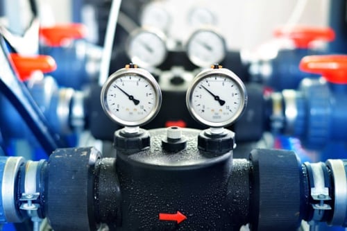Manometrar och ventiler på ett industriellt rörsystem med blå och röda komponenter.