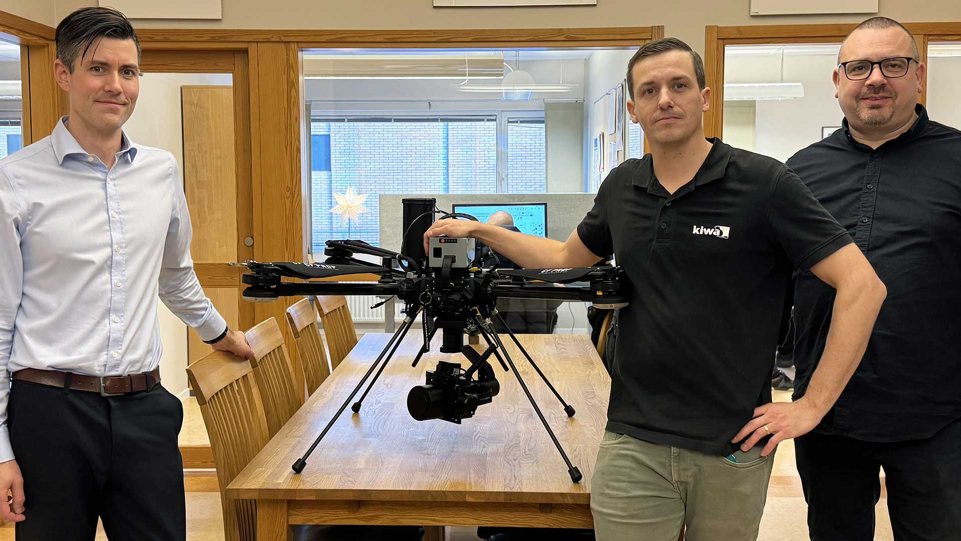 Tre personer från Kiwa står runt Tundra-drönaren på ett mötesbord i vårt kontor.