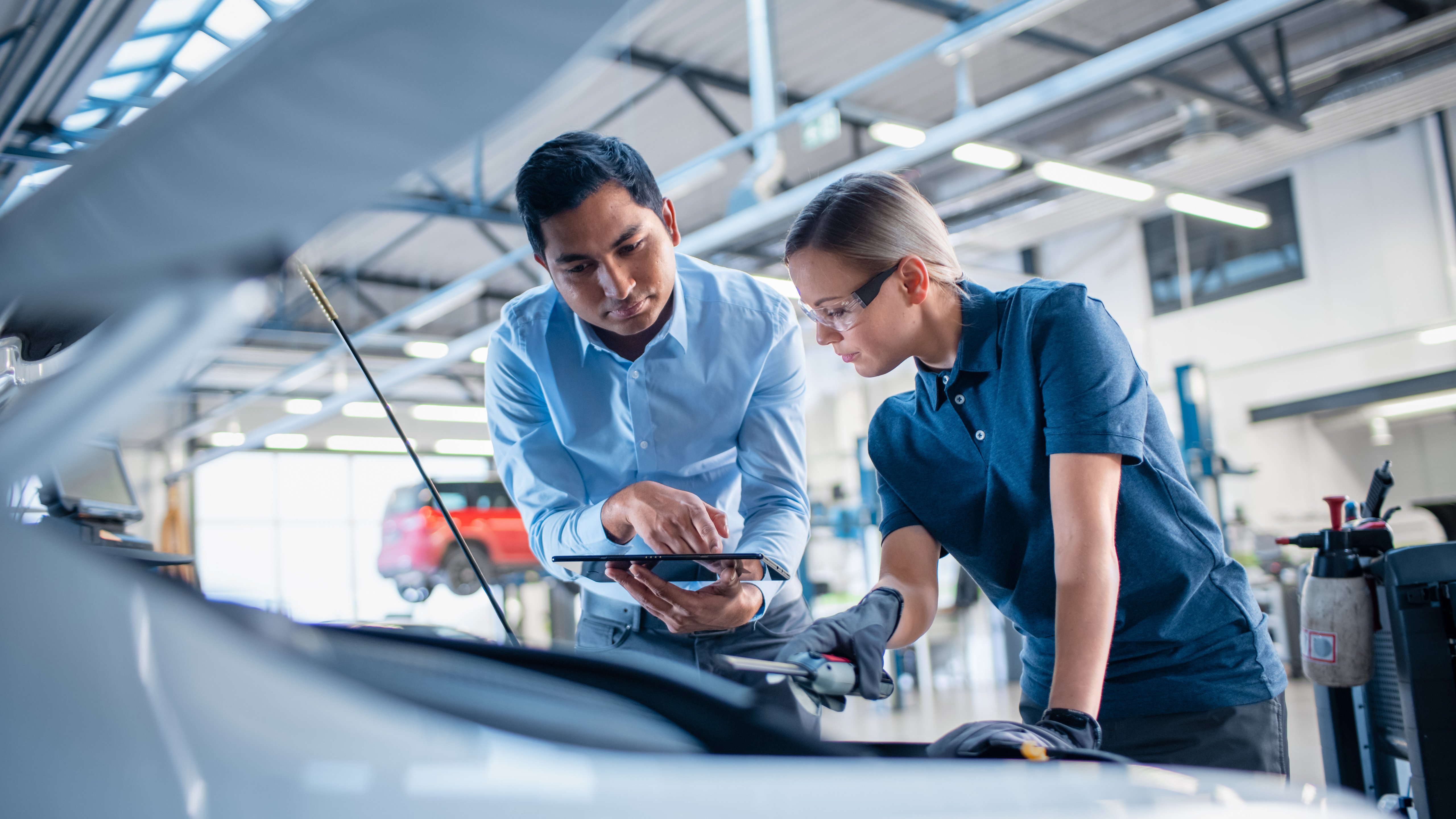 An automotive technician and an engineer collaborating on a vehicle inspection in a garage