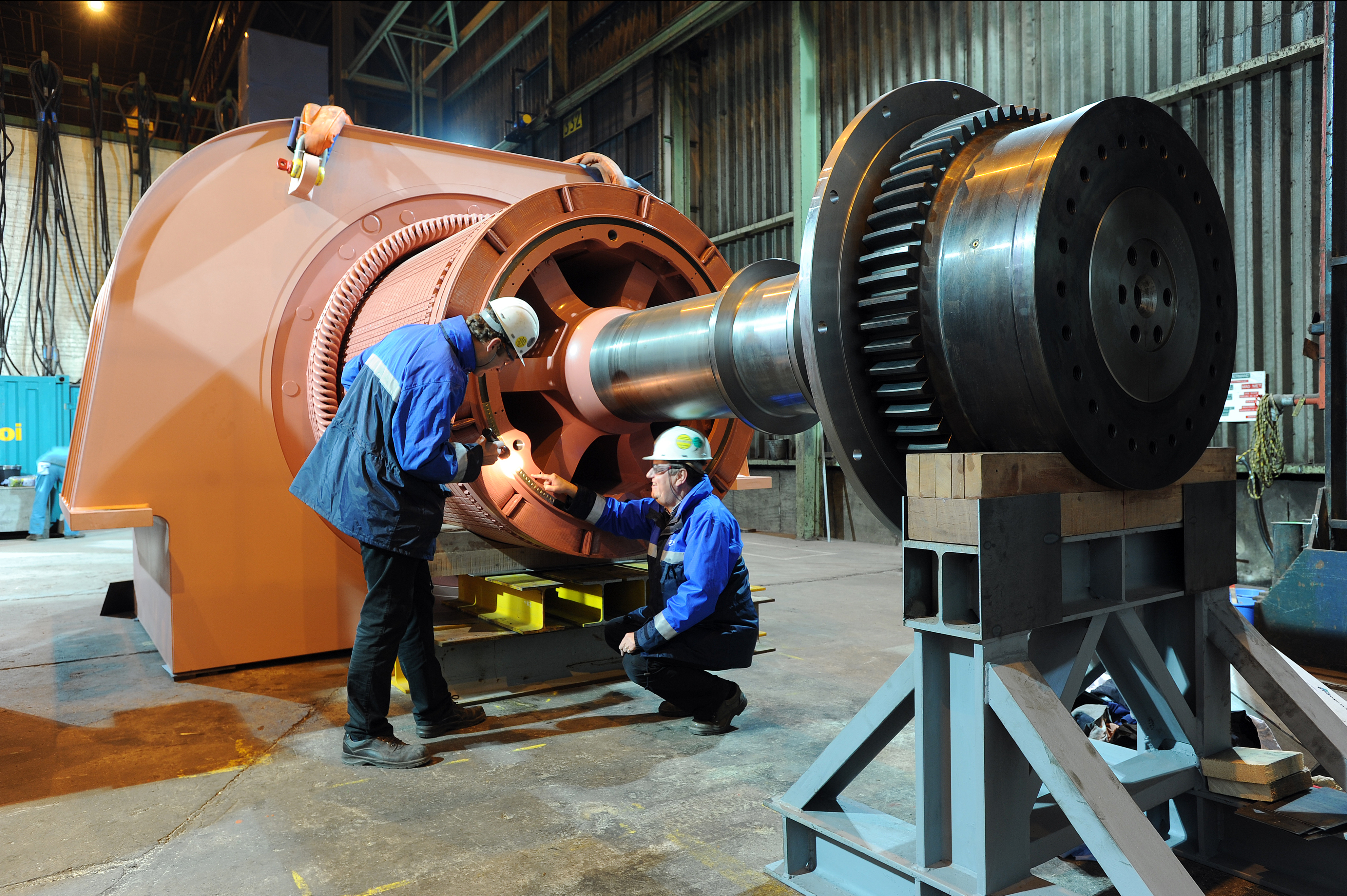 Two Kiwa PPI engineers in hard hats inspecting a large industrial turbine or generator assembly inside a factory workshop.