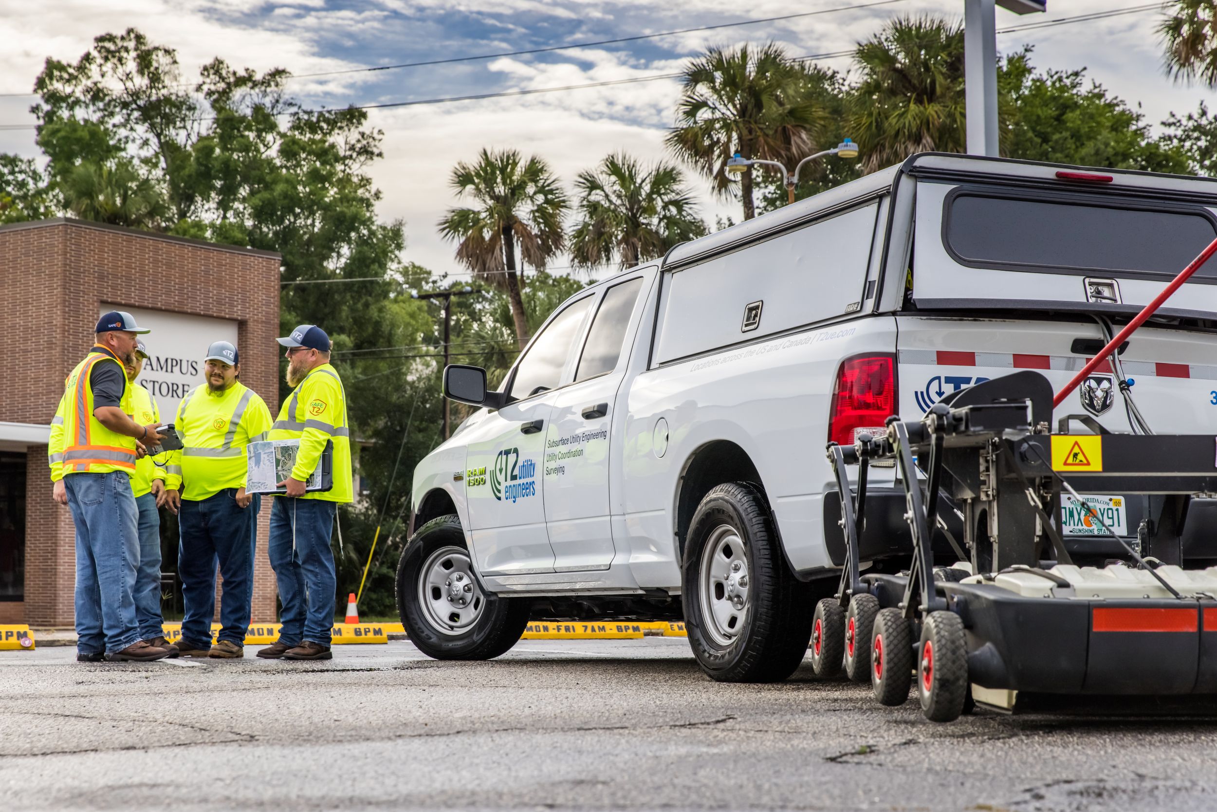 Kiwa employees in high-visibility safety vests stand beside a white utility pickup truck and equipment trailer at an outdoor work site.